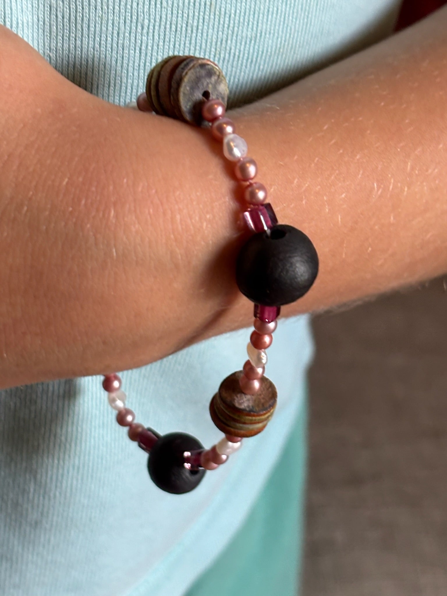 Close-up of a wrist wearing a beaded bracelet with dark beads and pink accents.